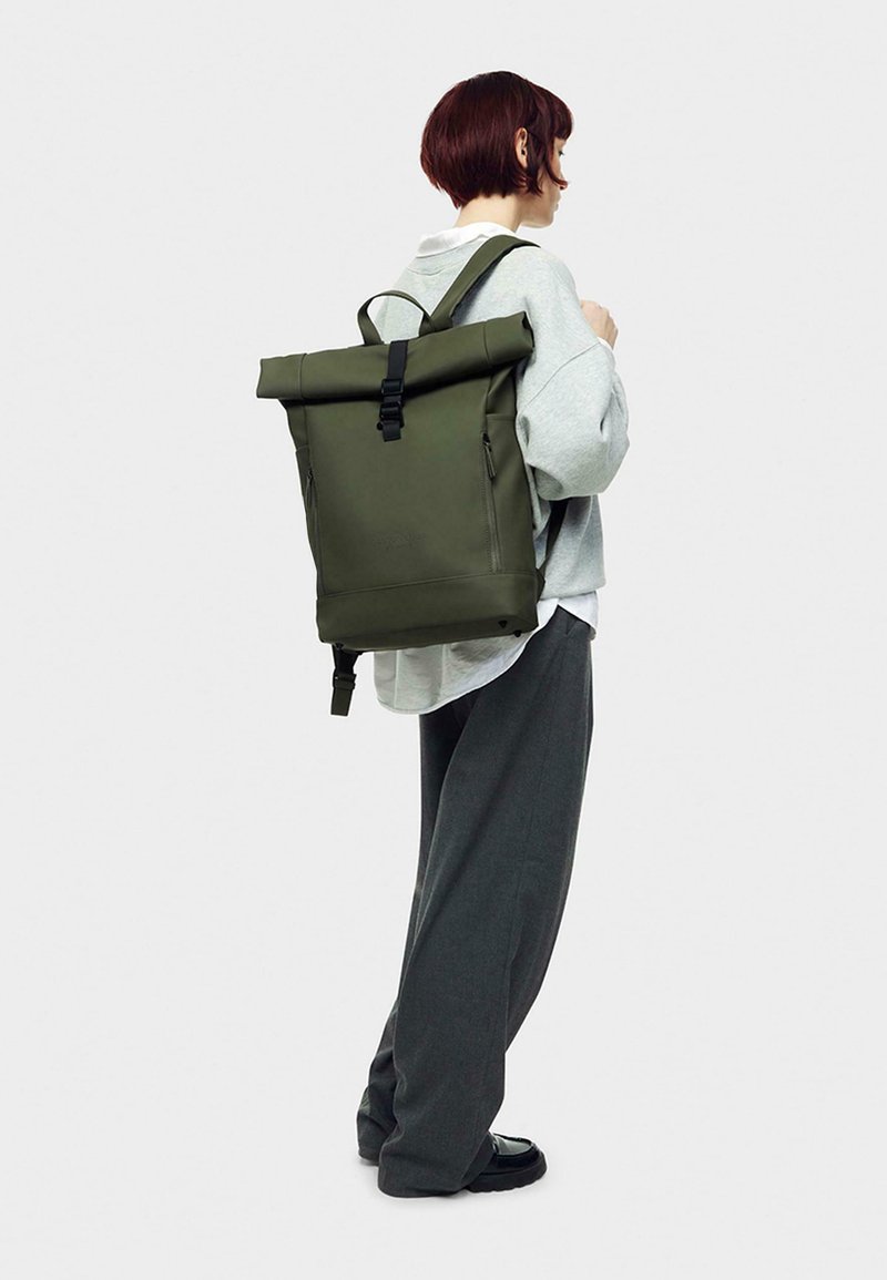 Olive green roll-top backpack with a black buckle and side zippers, made of durable material, featuring adjustable shoulder straps.