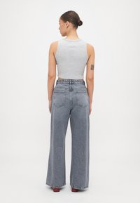 Grå avkortet tanktopp i kombinasjon med vide grå denimjeans med høy midje og baklommer; glatt tekstur, minimal detaljer.