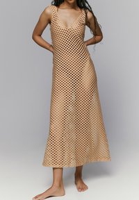 Vestido midi sin mangas en color beige, elaborado con un diseño de tricot abierto en forma de rejilla, con un escote en V profundo. Textura suave y un corte holgado.