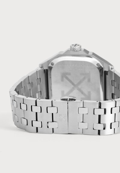 Gros plan sur une montre-bracelet en métal argenté, montrant son bracelet à maillons, son fermoir et le dos du boîtier.