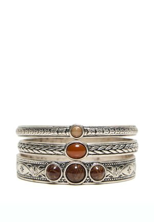 Trois bracelets argentés empilés avec des gravures détaillées, chacun présentant des pierres marron ovales ou rondes polies au centre.