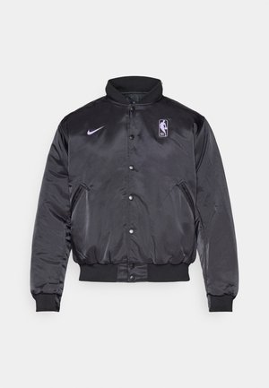 Sort satin bomberjakke med høj krave, trykknaplukning, NBA-logo og Nike-swoosh i lilla. Ribbestrikkede mansjetter og kant synlige.
