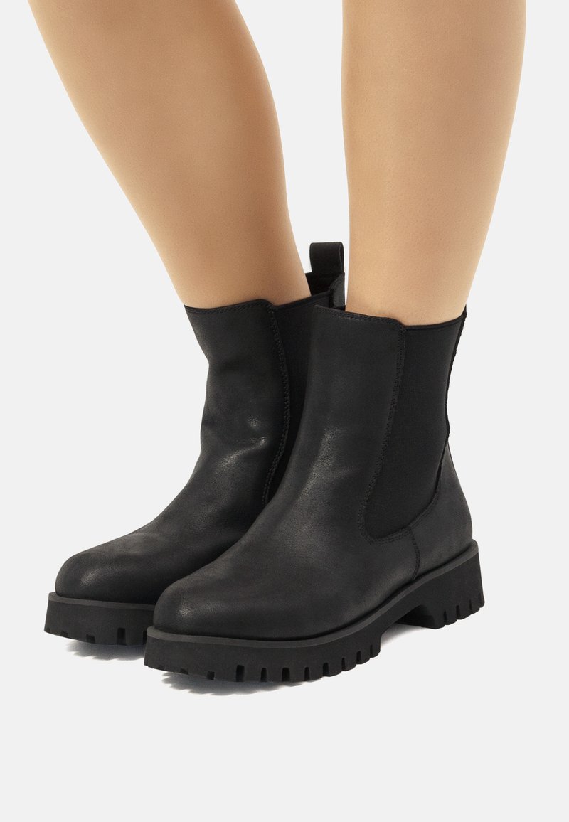 Botas de cuero negro hasta el tobillo con paneles laterales elásticos, punta redonda y suela de goma gruesa con un patrón de relieve y una pestaña en la parte posterior.