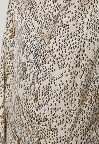 Tissu avec une base beige et un motif abstrait composé de petites formes irrégulières noires, marron et jaune clair évoquant un motif de peau de serpent.