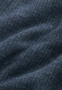 Tumma sininen neulottu kangas, jossa on pehmeä, teksturoitu pinta ja hienovaraisia värivaihteluita, taitettuna lempeisiin aaltoihin.