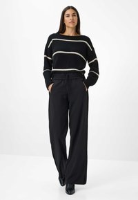 Pull à rayures noires avec des lignes blanches, pantalon noir taille élastique à jambes larges, porté avec des bottines noires à talons, texture lisse.