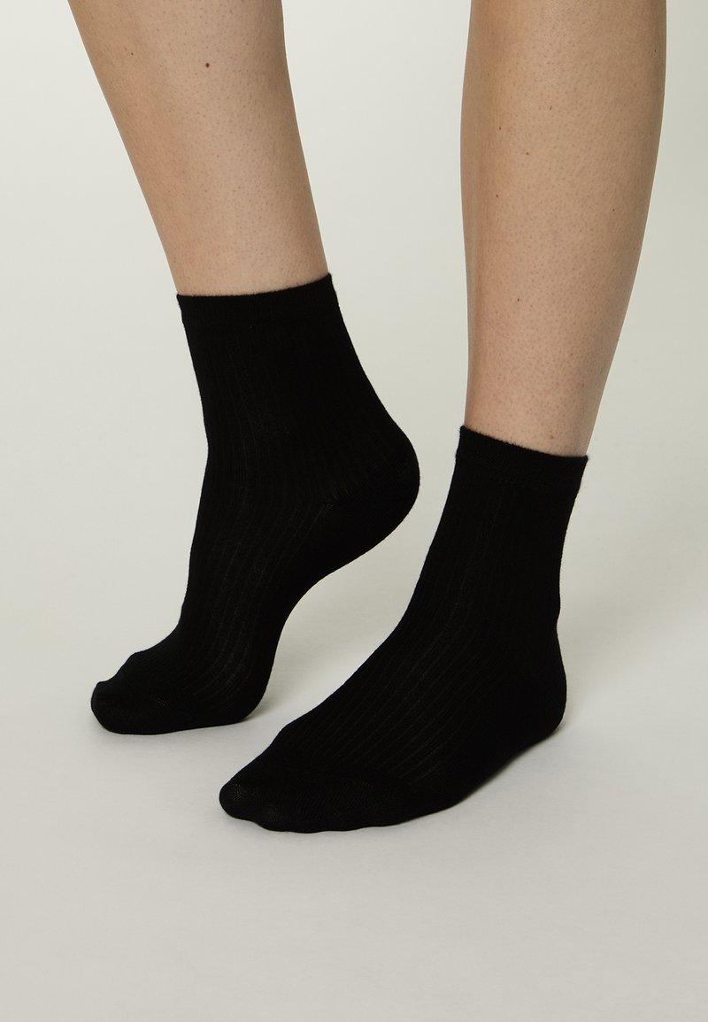 Schwarze, gerippte Socken aus weichem Stoff. Knöchellanges Design mit engem Bündchen und glatter Textur, ausgestattet mit einem klassischen Strickmuster.
