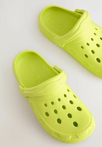 Lime zöld klumpák, könnyű anyagból készült, szellőzőlyukakkal, puha pánttal és texturált talpbetéttel a kényelem érdekében.