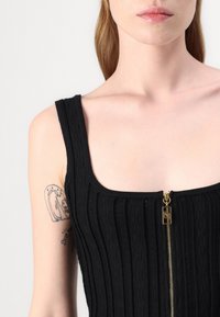 Μαύρο αμάνικο μπλουζάκι με ριγωτή υφή και χρυσό φερμουάρ στη μέση. Ο λαιμός έχει τετράγελλη μορφή, με φαρδιές στράπες και χωρίς εμφανή σχέδια.