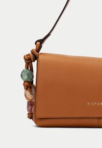 Brązowa torebka crossbody z teksturowanej skóry, z węzłowym paskiem zdobionym kolorowymi koralikami w zielonym, beżowym i różowym kolorze.