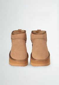 Tan suede ankle boots featuring a rounded toe, stitched accents, and a light brown rubber sole, with a soft interior lining.