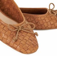 Geweven leren balletschoenen in een warme tan kleur, met een ronde neus, bruine veters en een gestructureerd patroon op het bovenmateriaal.