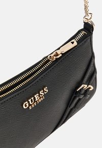 Borsa a tracolla sintetica nera con finitura testurizzata, hardware dorato, chiusura superiore a cerniera e dettaglio accentato annodato. Presenta il logo del marchio impresso sul lato.