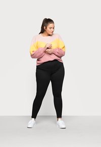 Knit sweater with pink and yellow chevron pattern, paired with black leggings and white sneakers. Casual fit, textured fabric.