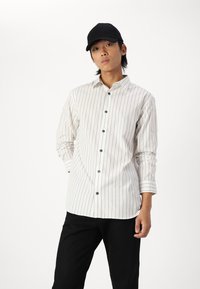 Witte overhemd met verticale grijze streepjes. Kenmerkt zich door een spread collar en lange mouwen. Draag het met een zwarte broek en een zwart pet.