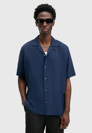 Marineblauwe kortmouwenshirt van gladde stof; heeft een kampkraag, zes knopen en een subtiel geborduurd logo op de linkerkant van de borst.