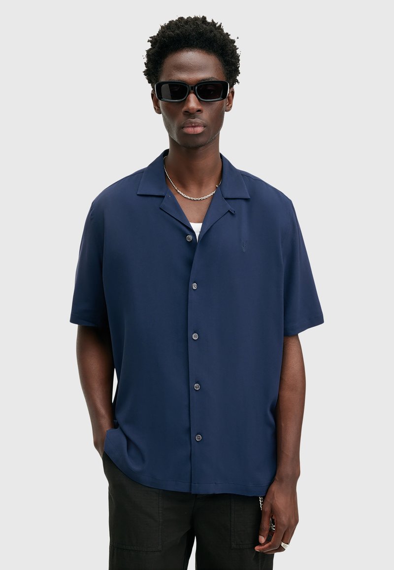 Marineblauwe kortmouwenshirt van gladde stof; heeft een kampkraag, zes knopen en een subtiel geborduurd logo op de linkerkant van de borst.