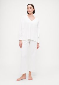 White knit loungewear set featuring a V-neck oversized top and wide-leg pants. Soft texture with a relaxed fit, minimal stitching details.