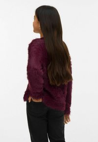 Bordo mākslīgās kažokādas džemperis ar fakturētu, pūkainu virsmu, garām piedurknēm un vaļīgu piegriezumu, kombinēts ar melnām džinsa biksēm.