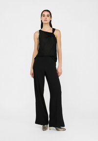 Black sleeveless top features a knotted design and shiny accents, paired with black wide-leg pants and metallic patterned shoes.