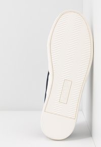 Semelle d'une basket en caoutchouc blanche avec une adhérence texturée et "Lauren Ralph Lauren" embossé au centre.