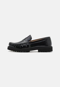 Mocassin en cuir noir avec un bout rond, couture textur�ée et une semelle en caoutchouc présentant des crampons proéminents pour l'adhérence et la durabilité.