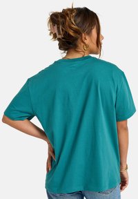 Turquoise oversized t-shirt with short sleeves, round neck, and soft cotton fabric. Back view shows relaxed fit and seam detailing.