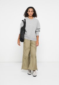 Šedá mikina s rebrovanými manžetami, khaki cargo nohavice s veľkými vreckami a čierna taška cez rameno. Tenisky dopĺňajú neformálny outfit.