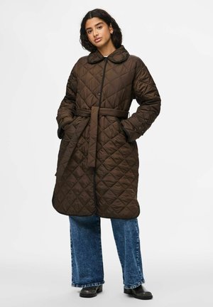 Manteau d'hiver matelassé marron avec un col, taille ceinturée et poches latérales. Associé à un jean bleu à jambes larges et des bottes noires.