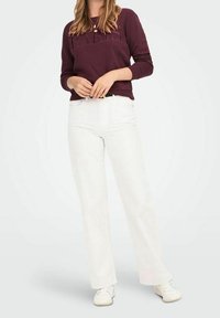 Felpa color bordeaux con testo "PARIGI", abbinata a jeans bianchi a gamba larga. Design minimalista, texture morbida e sneaker bianche casual completano il look.