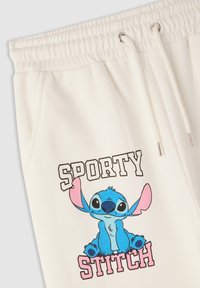 Białe dresy z elastycznym pasem, z niebieską grafiką Stitcha i czarnym napisem 'SPORTY' nad różowym napisem 'STITCH'.