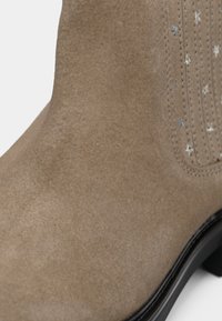 Bottine en daim marron clair avec broderie d'étoile argentée et semelle noire sur fond blanc.