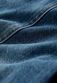 Sötétkék denim anyag, amelynek textúrája látható szövés és elkészült varrások. Az anyagnak lágy esése van és enyhe fényessége.