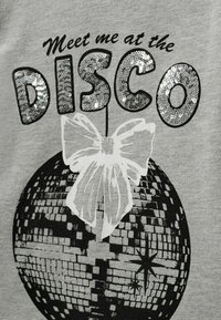 Sivá tričko s čierno-bielou diskovou guľou a bielou mašľou, obklopené žiarivým strieborným textom so znakom "Stretneme sa na DISCO."