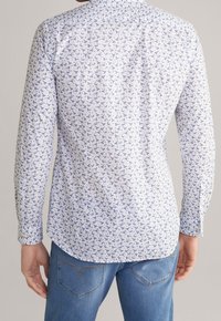Wit shirt met lange mouwen met een patroon van blauwe vogels, voorzien van een puntige kraag en een afgeronde zoom, gecombineerd met blauwe denim jeans.