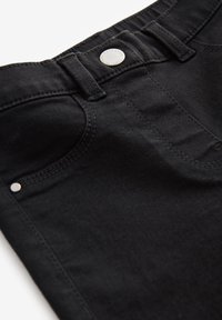 Jeans de mezclilla negra con cierre de botón, diseño de cinco bolsillos y detalles de costura sutiles. La tela tiene una textura suave y un acabado mate.