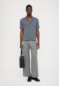 Short-sleeve gray polo shirt with a green button placket, paired with wide gray trousers and a black bag, worn with black shoes.
