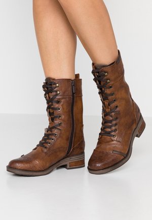 Braune Leder-Ankle-Boots mit Schnürung und seitlichem Reißverschluss, strukturierten Details an der Zehenpartie und flachen Holzsohlen.
