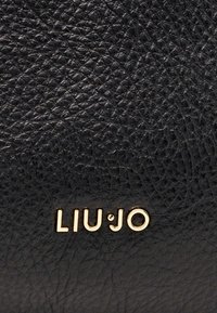 Sac à main en cuir noir texturé présentant un logo doré "LIU·JO" proéminent sur le devant, avec une surface en relief et à motif.