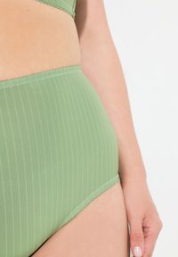 Hoge taille groene stoffen slip met verticale strepen, gladde textuur en een gegolfde tailleband. Close-up weergave van detail en pasvorm.