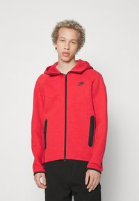 Felpa rossa con zip e cappuccio, dettagli in zip nera e tasche laterali. Realizzata in tessuto testurizzato, presenta un piccolo logo nero sul petto.