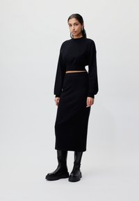 Svart strikket kort genser og høyt liv skjørt, kombinert med knelengde svarte støvler. Glatt tekstur, tettsittende design, minimalistisk stil.