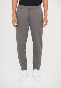 Graue Jogginghosen mit elastischem Bund und Kordelzug, ausgestattet mit Seitentaschen und gerippten Bündchen. Dazu weiße Sneakers.