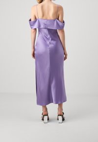 Tylny widok kobiety w lawendowej, satynowej sukience bez ramiączek z cienkimi paskami oraz czarno-białych sandałach na słupku.