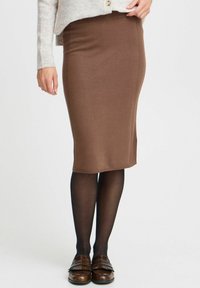 Jupe crayon marron en tricot avec texture côtelée verticale, longueur genou, assortie avec des collants noirs et des mocassins à franges marron.