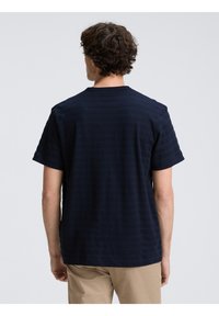 Camiseta de manga corta azul marino con un patrón de rayas texturadas y cuello redondo, vista desde la parte de atrás. Adecuada para uso casual.