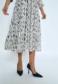 Une longue robe fluide avec un motif en zigzag noir, blanc et pêche ; chaussures à talons hauts noires sans détails, avec des bouts pointus.