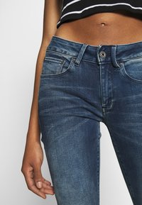 Úzké modré džíny z denimu s bledým vzhledem, pětipocket designem, kovovým zapínáním a jemnými švy.