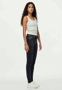 Calças de ganga pretas ajustadas em material denim elástico, combinadas com uma t-shirt cinza justa e ténis brancos. O conjunto apresenta um design simples.