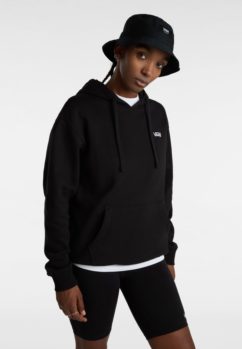 Zwarte katoen hoodie met een kangoeroenzak en koorden, gedragen over een wit shirt, gecombineerd met zwarte shorts en een zwarte bucket hat.